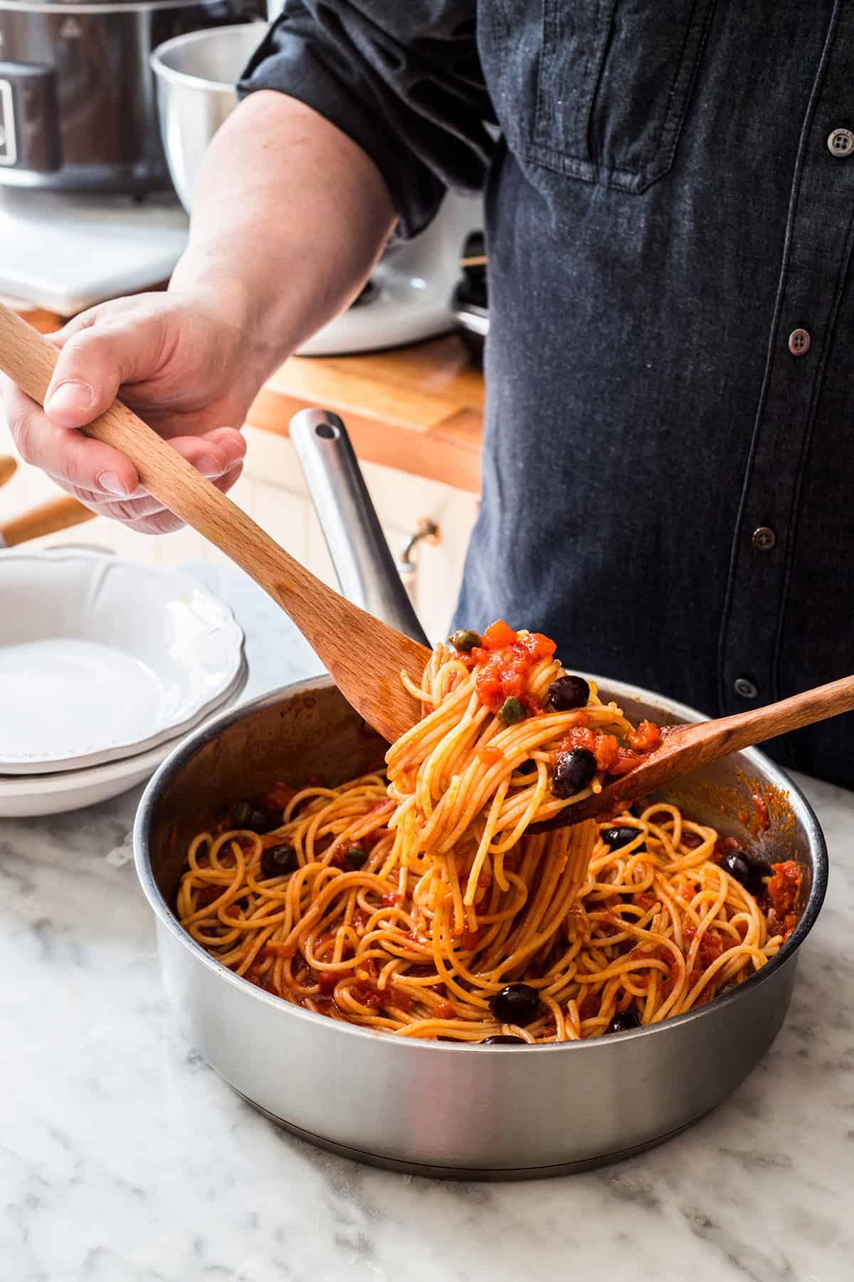 A man tossing spaghetti with vegan puttanesca sauce.