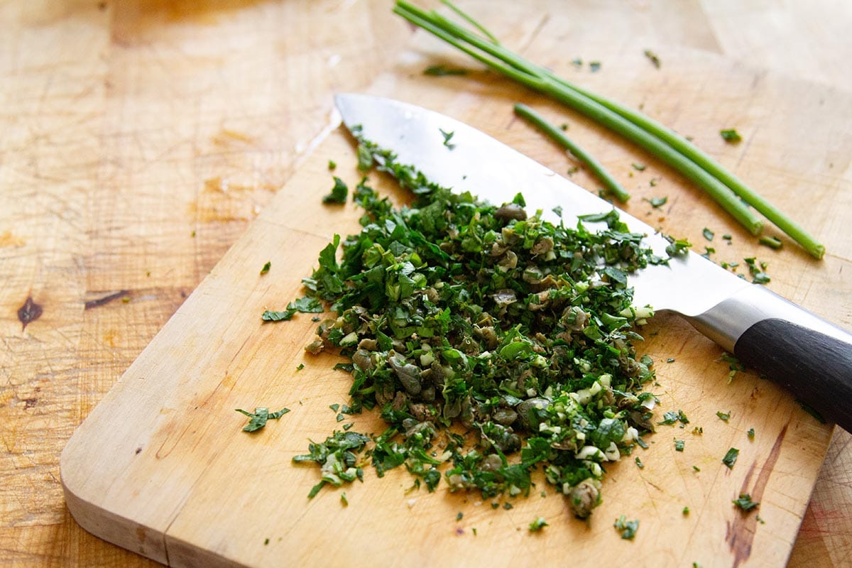 Chopped fresh herbs in a cutting board with a knife aside.