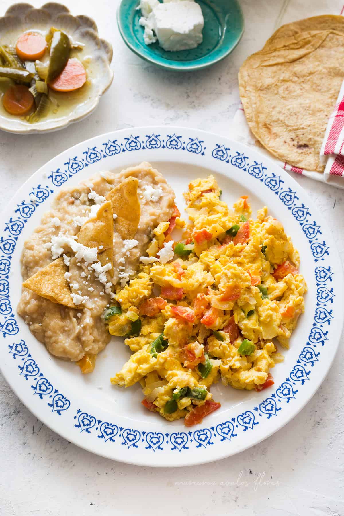 Huevos a la mexicana (scrambled eggs mexican style) served on a plate with refried beans, totopos and cheese.