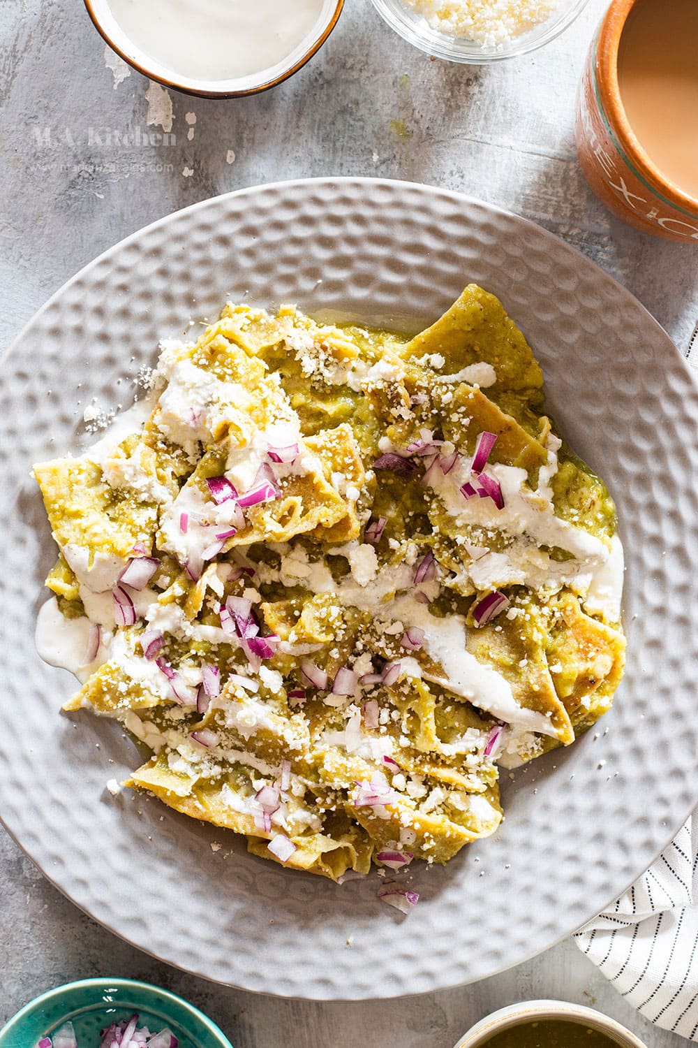 Mexican chilaquiles verdes served on a grey plate. Cheese, cream, and onions added as toppings.