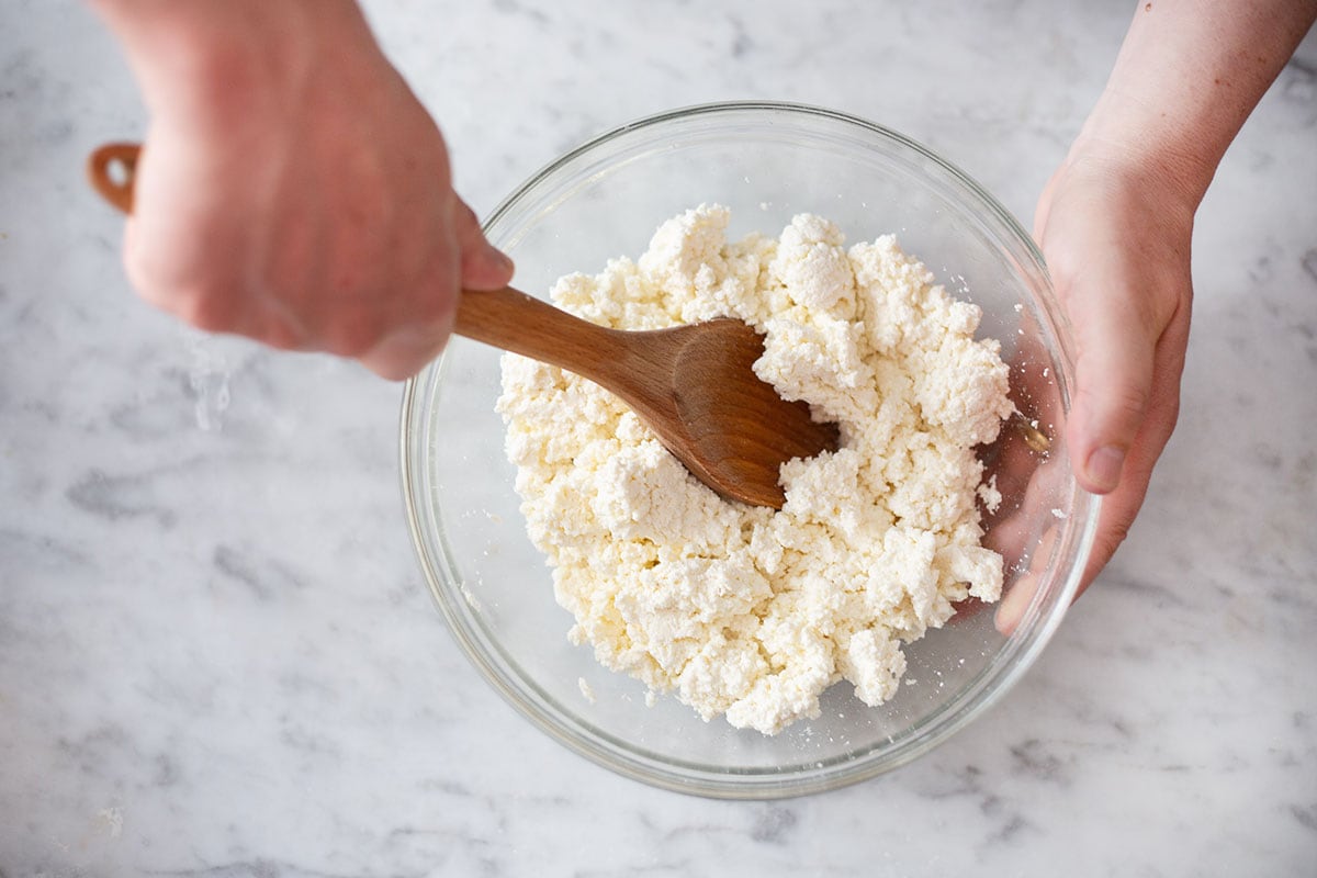 A person mixing queso fresco in a bowl.
