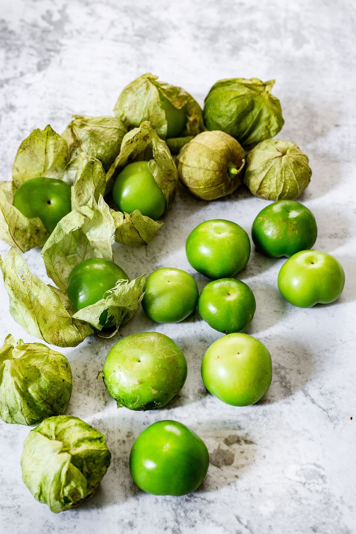 Fresh tomatillos scattered on a concrete surface.