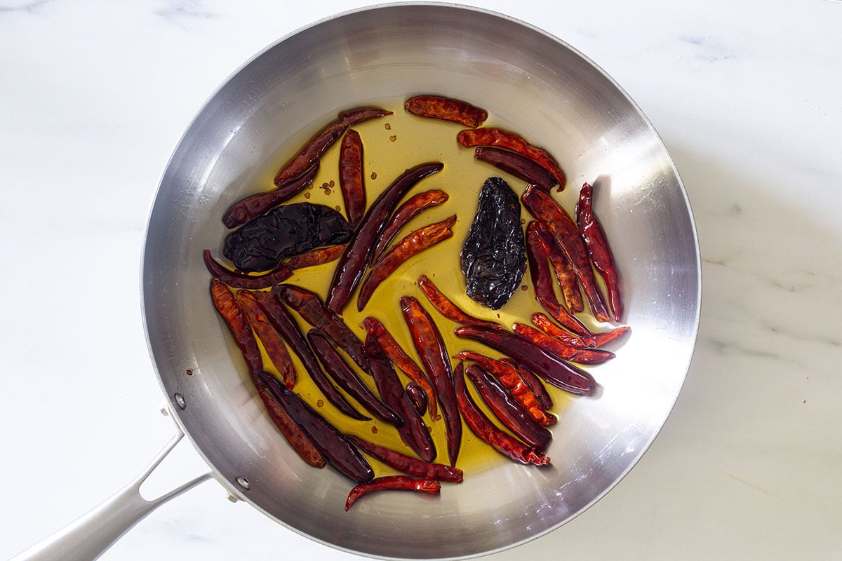 Chiles de árbol y chiles morita friéndose en una cazuela para mostrar como hacer salsa macha en casa.