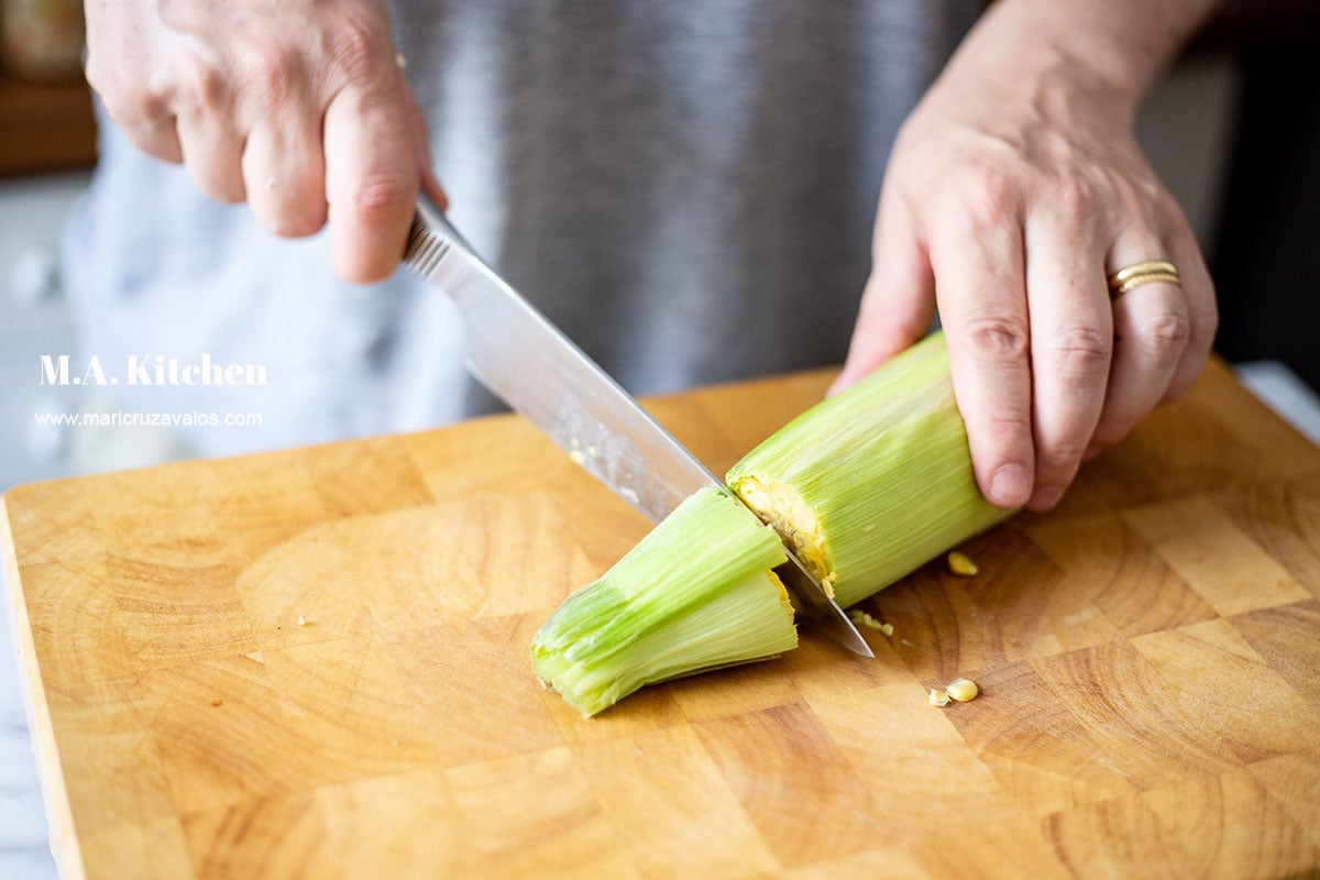 Cutting the end of a fresh corn ear with a knife.