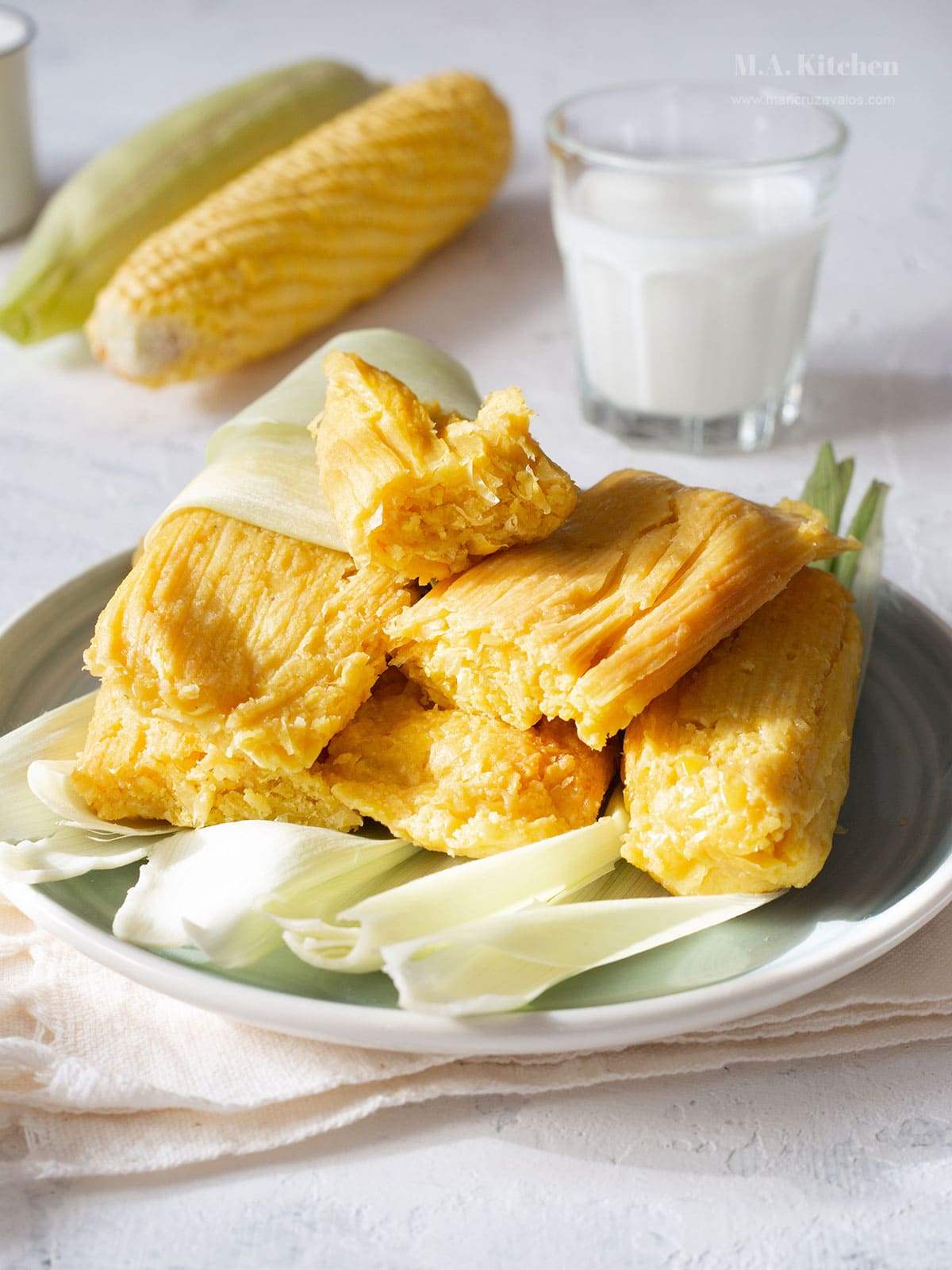 Tamales de elote unwrapped and placed on a place with a glass of milk and fresh corn ears on the background.