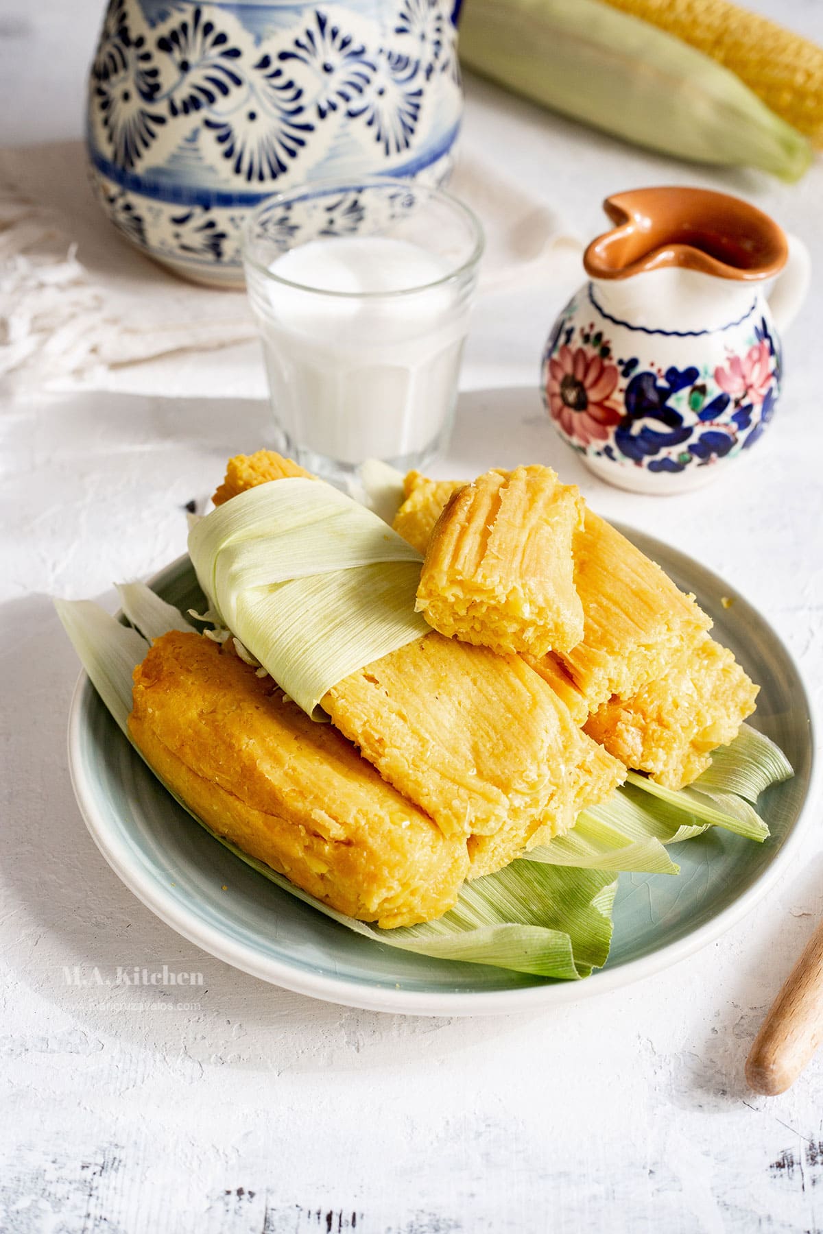 Sweet corn tamales de elote in a plate, unwrapped, and with a mug of coffee on the background.