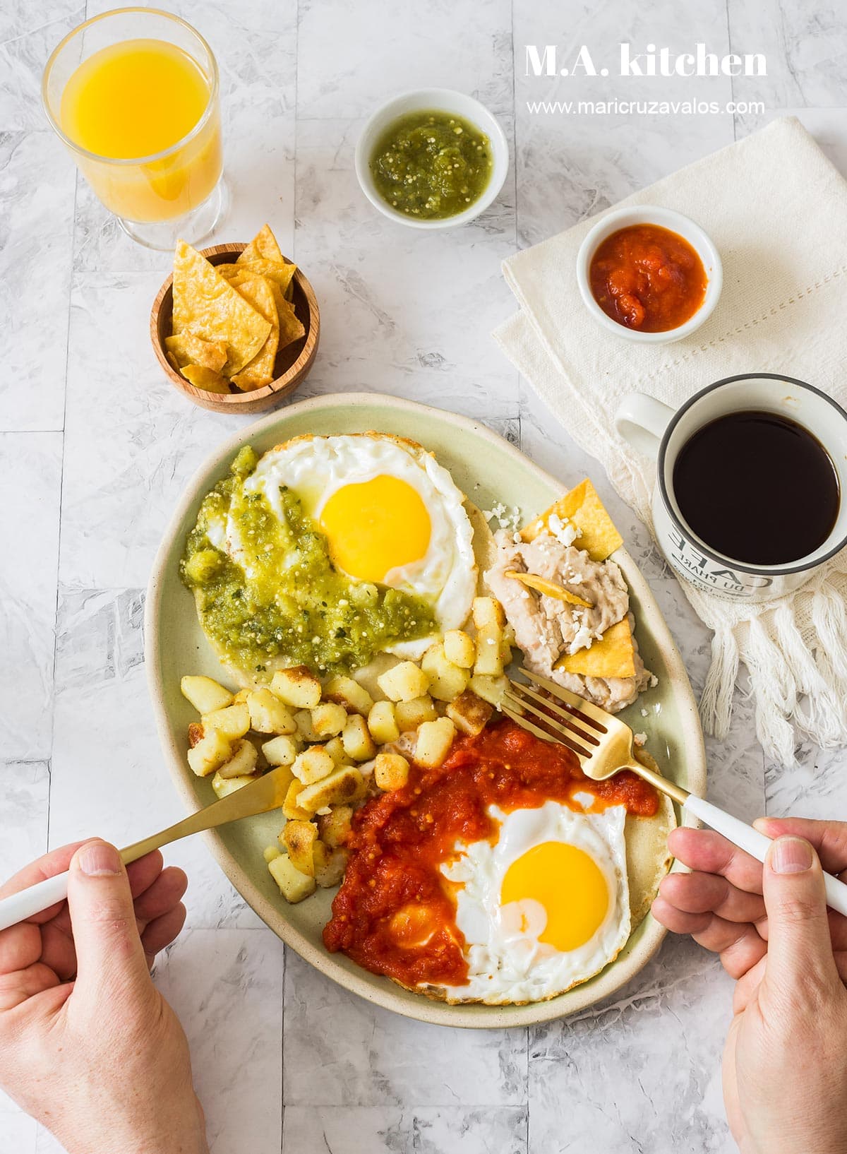 Man hands with utensils over huevos divorciados served with refried beans and potatoes. Around two bowls with salsas and corn chips, coffee, and orange juice on a glass.