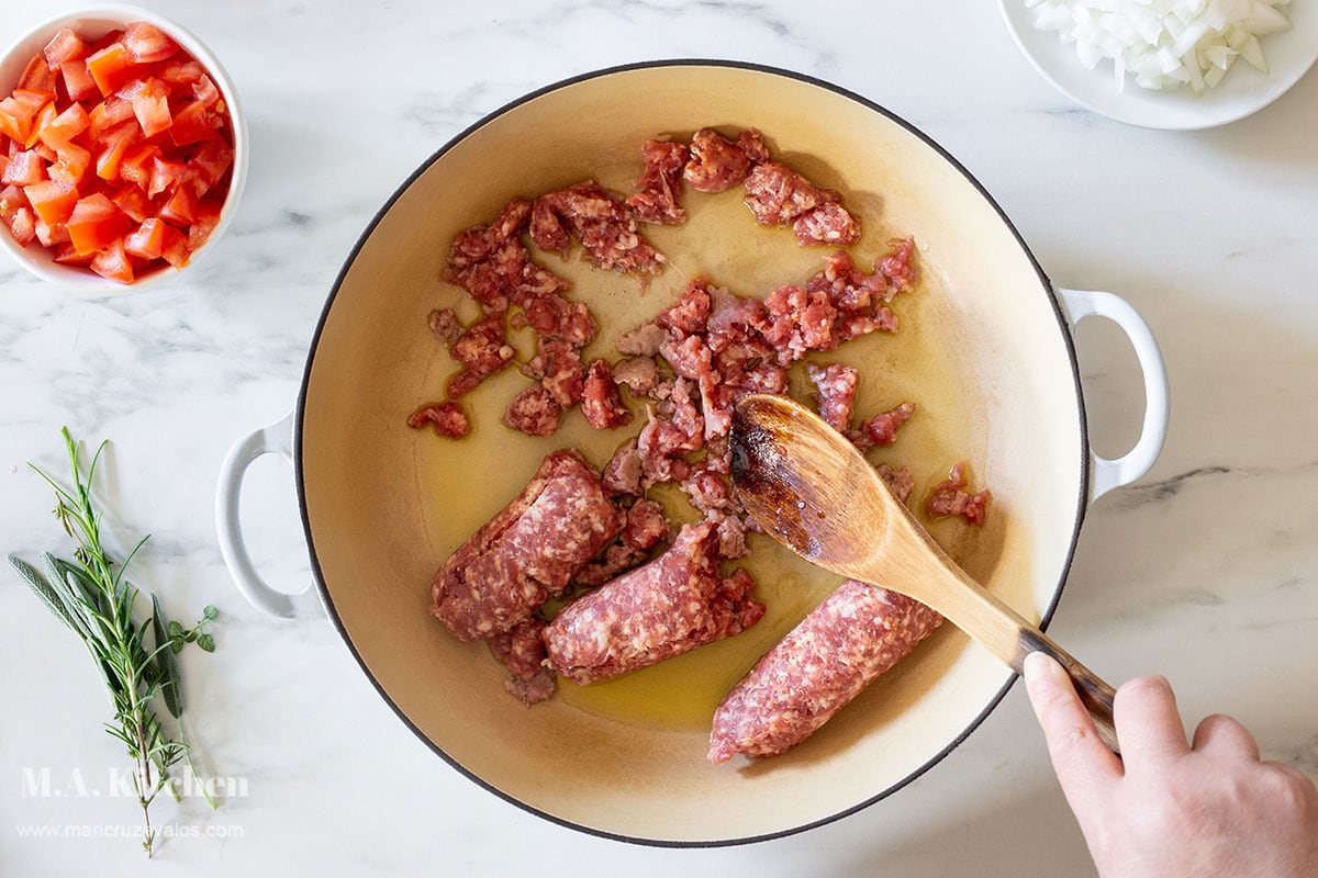 Breaking Italian sausage in a pan with a wooden spoon.
