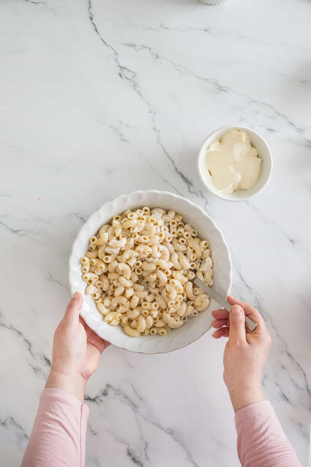 Coating macaroni with mayo on a bowl.