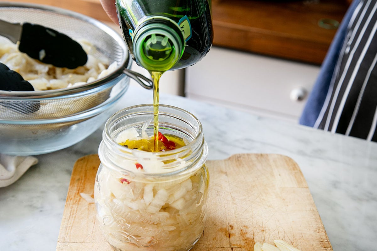 Pouring extra-virgin olive oil inside a jar with eggplant and seasonings.