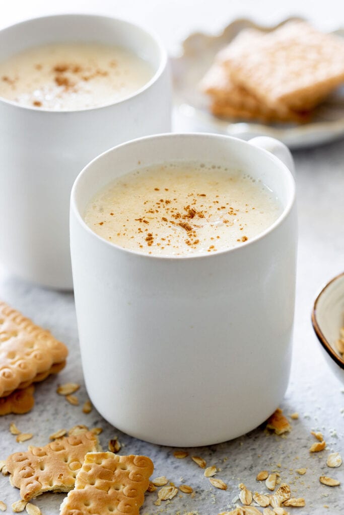 Atole de Avena, aka oatmeal atole served on white cups with powdered cinnamon sprinkled on top.