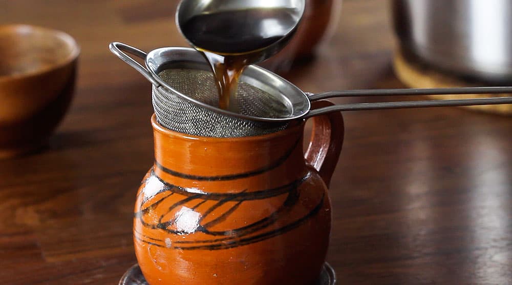 Straining the café de olla into a clay mug.