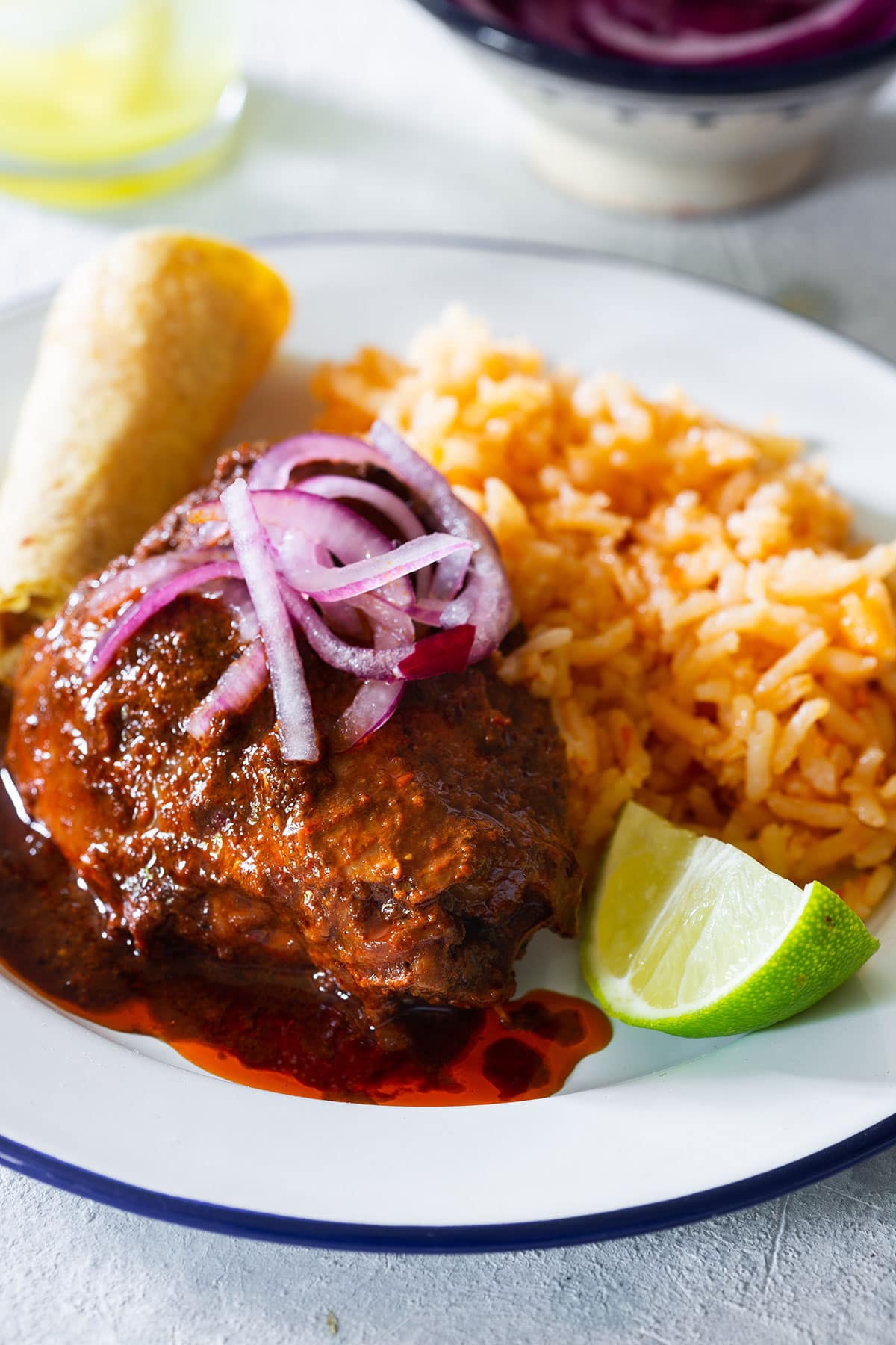 Mexican adobo chicken served in a plate topped with pickled onions and a side of Spanish rice.