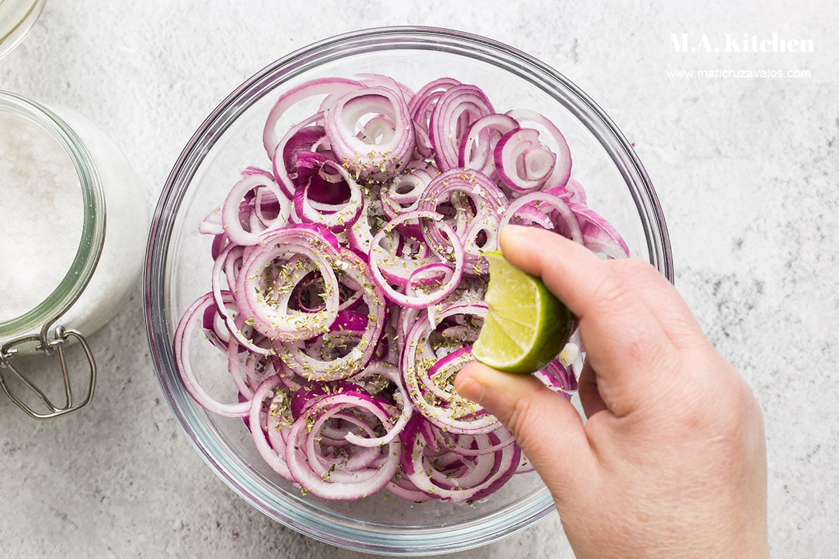 Squeezing a lime wedge over red onions in a bowl.