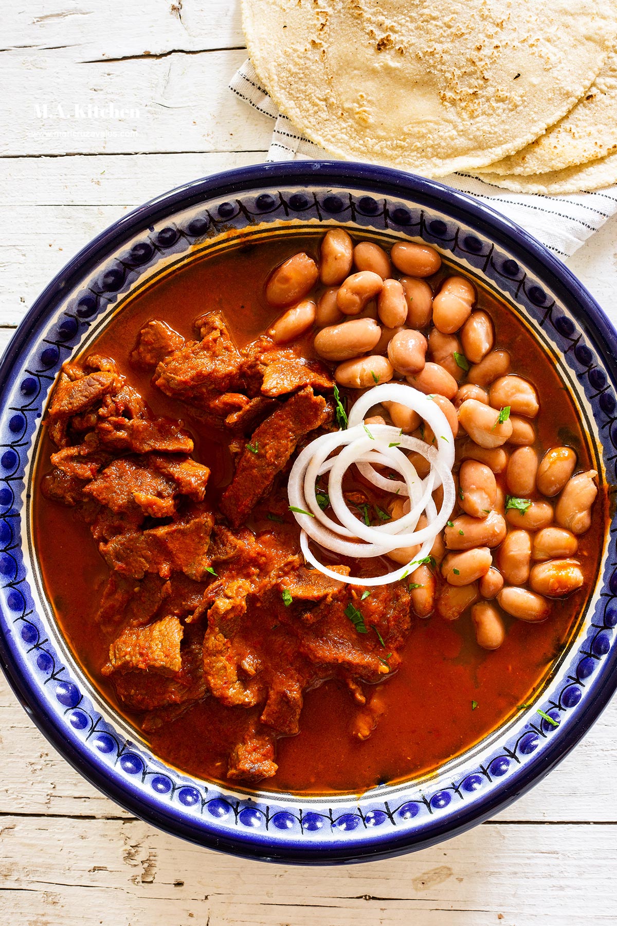 Beef chile rojo served with a side of beans and fresh sliced onion on top.