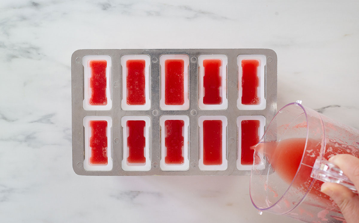 Filling molds with watermelon paletas mixture.
