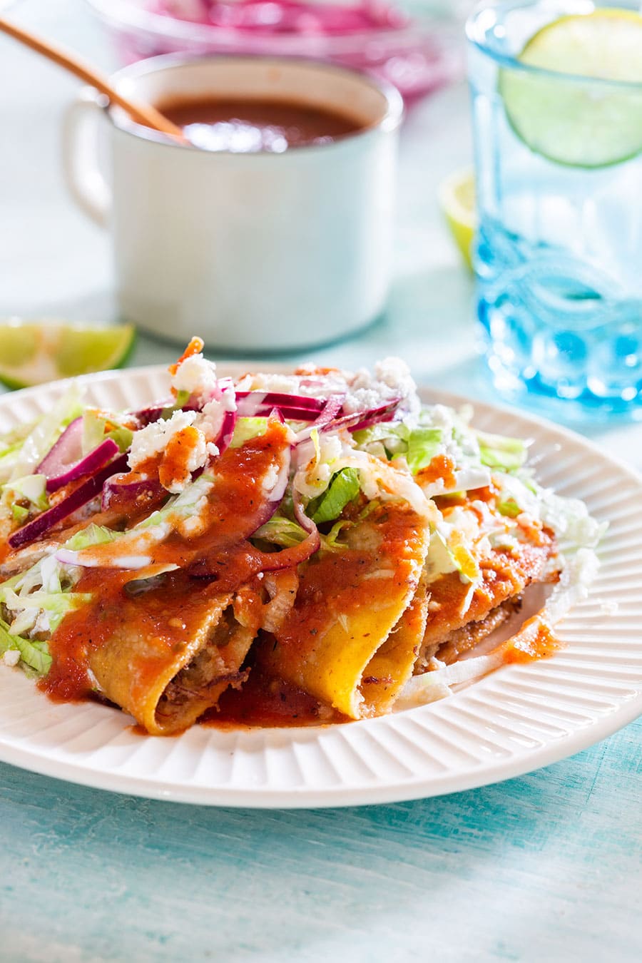 Deep fried tacos dorados in a plate topped with lettuce, sauce, onions, cheese, and cream.
