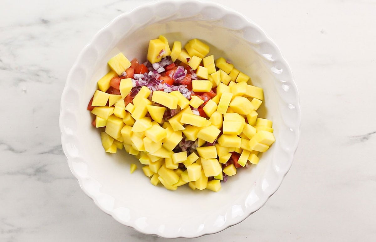 Diced mango on top of tomatoes and onions in a white bowl.