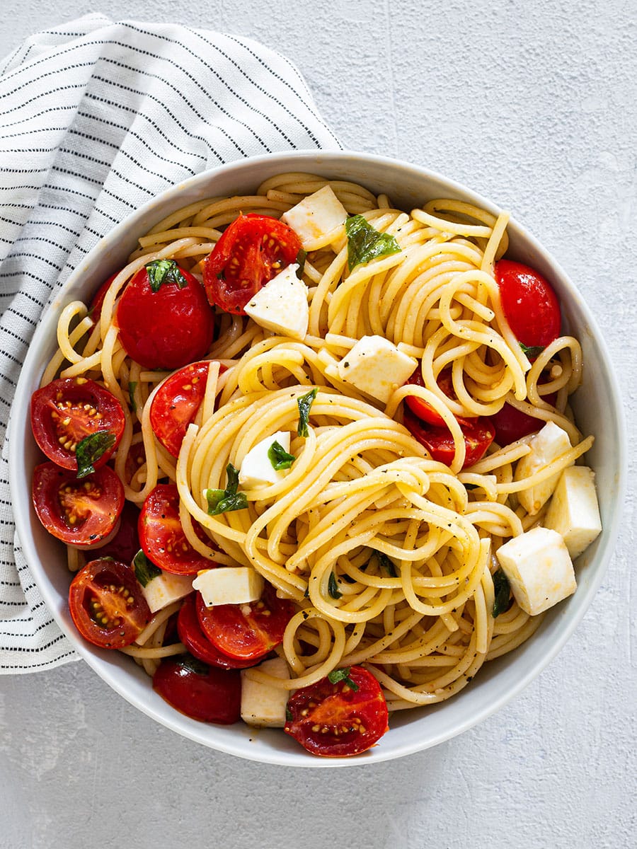 A plate with spaghetti tossed with cherry tomatoes, basil and mozzarella.