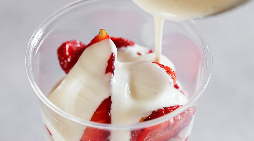 Pouring cream into a cup with strawberry slices.
