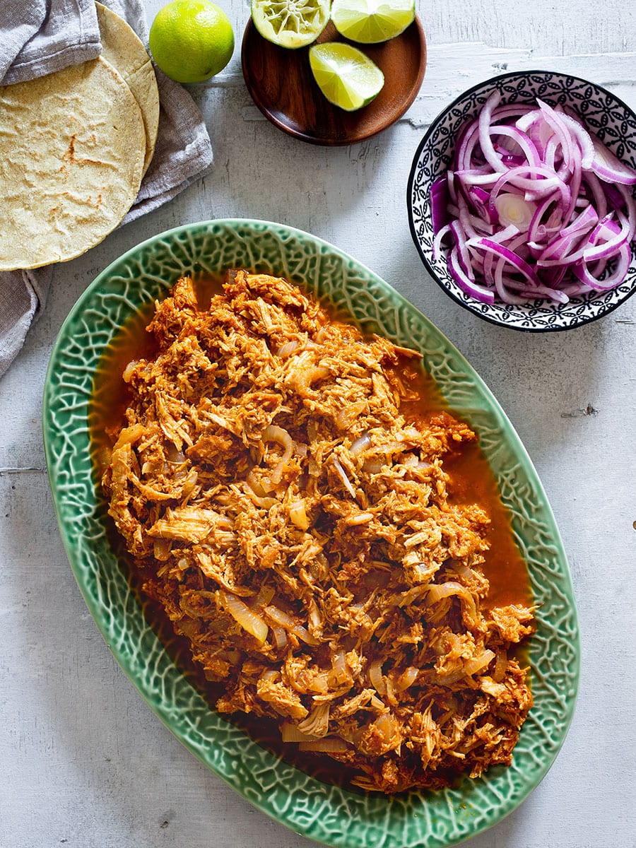 Tinga de pollo served on a platter. Pickled red onions, lime wedges and warm tortillas on the side.