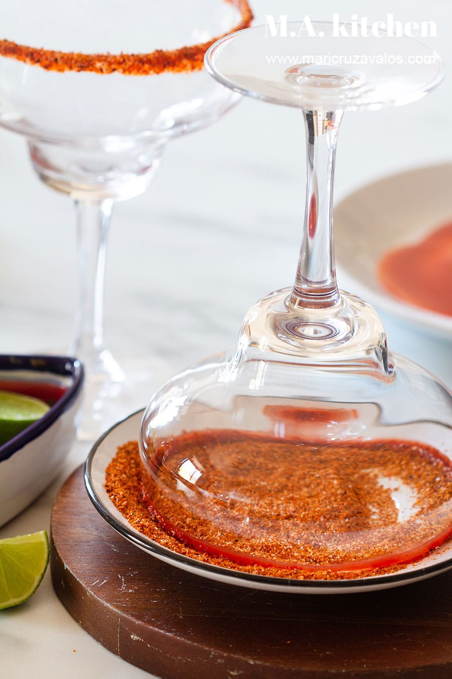 Dipping rims of a margarita glass on chili powder.