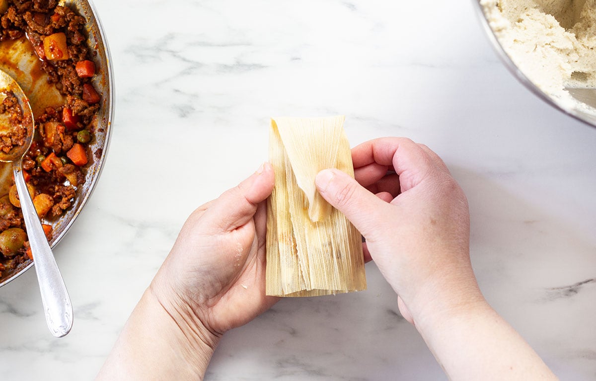 Folding the pointy edge of a tamal towards the middle.
