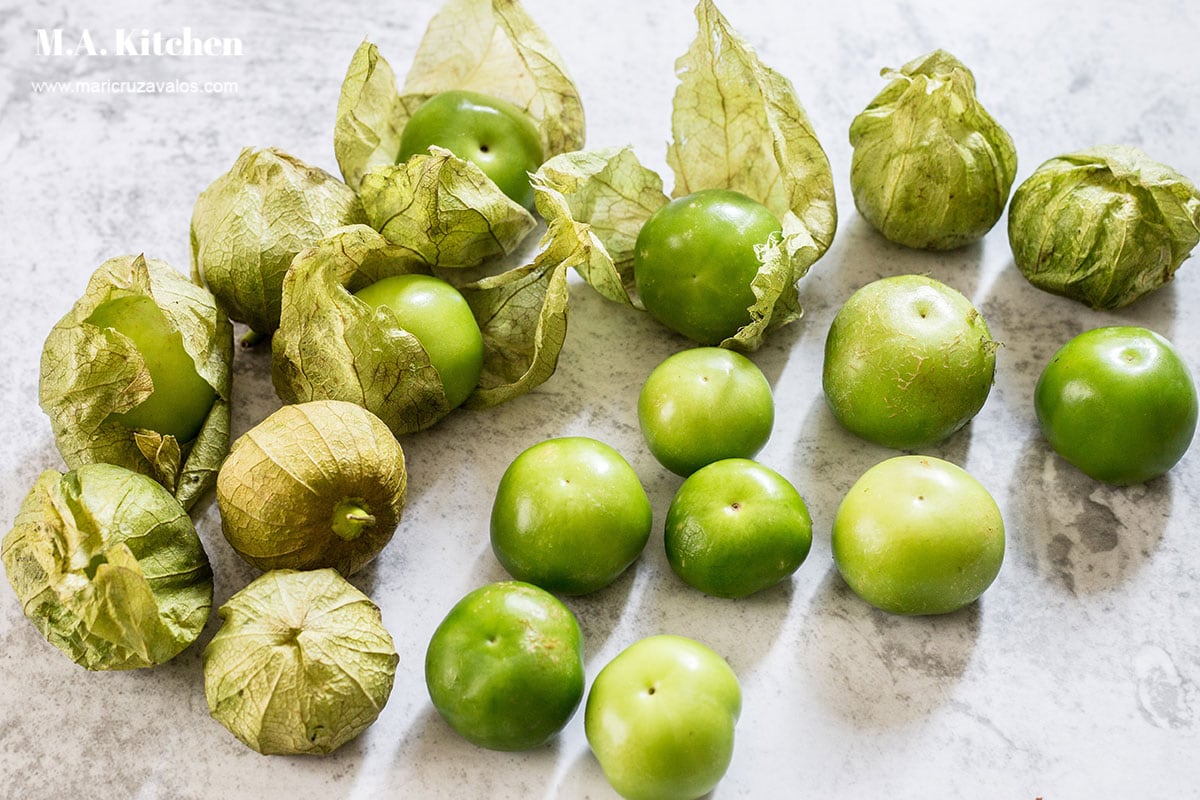 A bunch of tomatillos with and without husks displayed on a concrete surface.