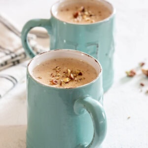 Square image of two turquoise mugs filled with creamy atole de nuez, topped with chopped toasted pecans, perfect for a traditional Mexican breakfast.