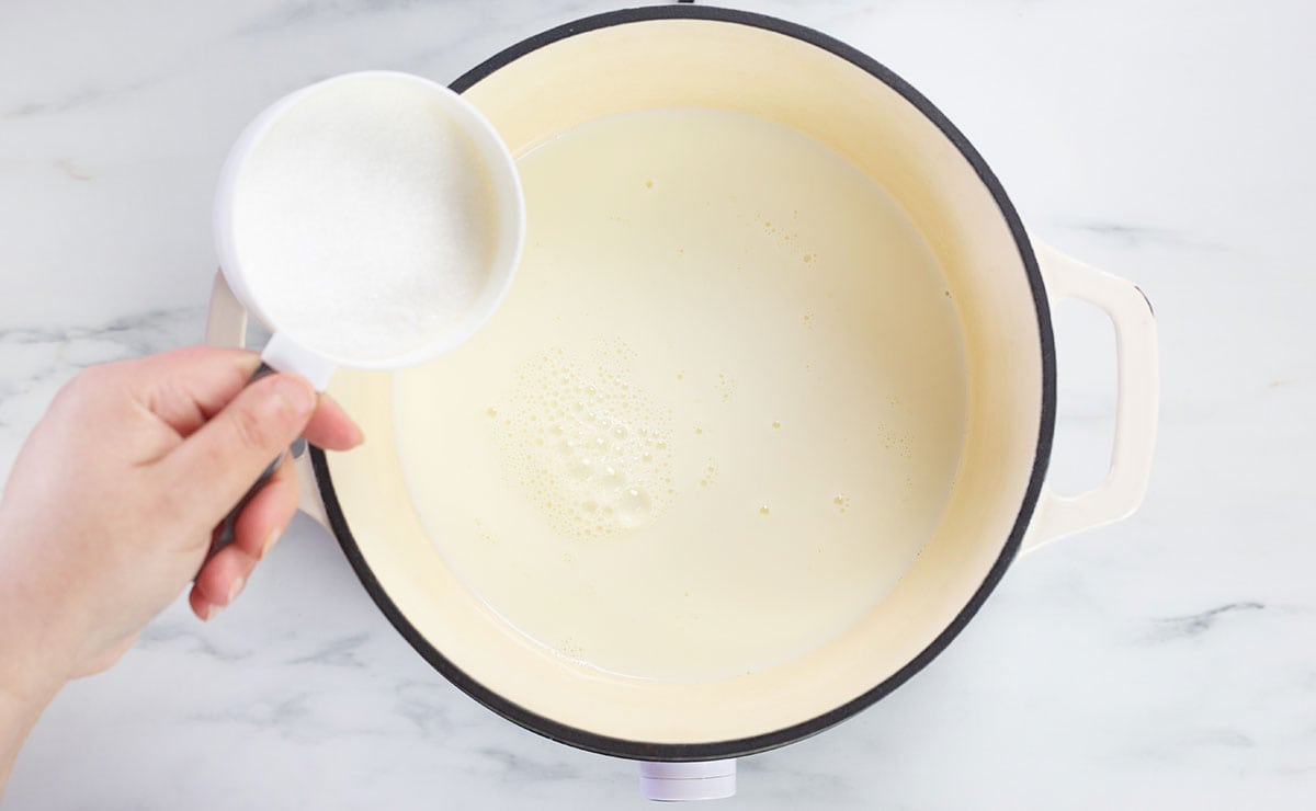 Adding sugar to the pot with milk.