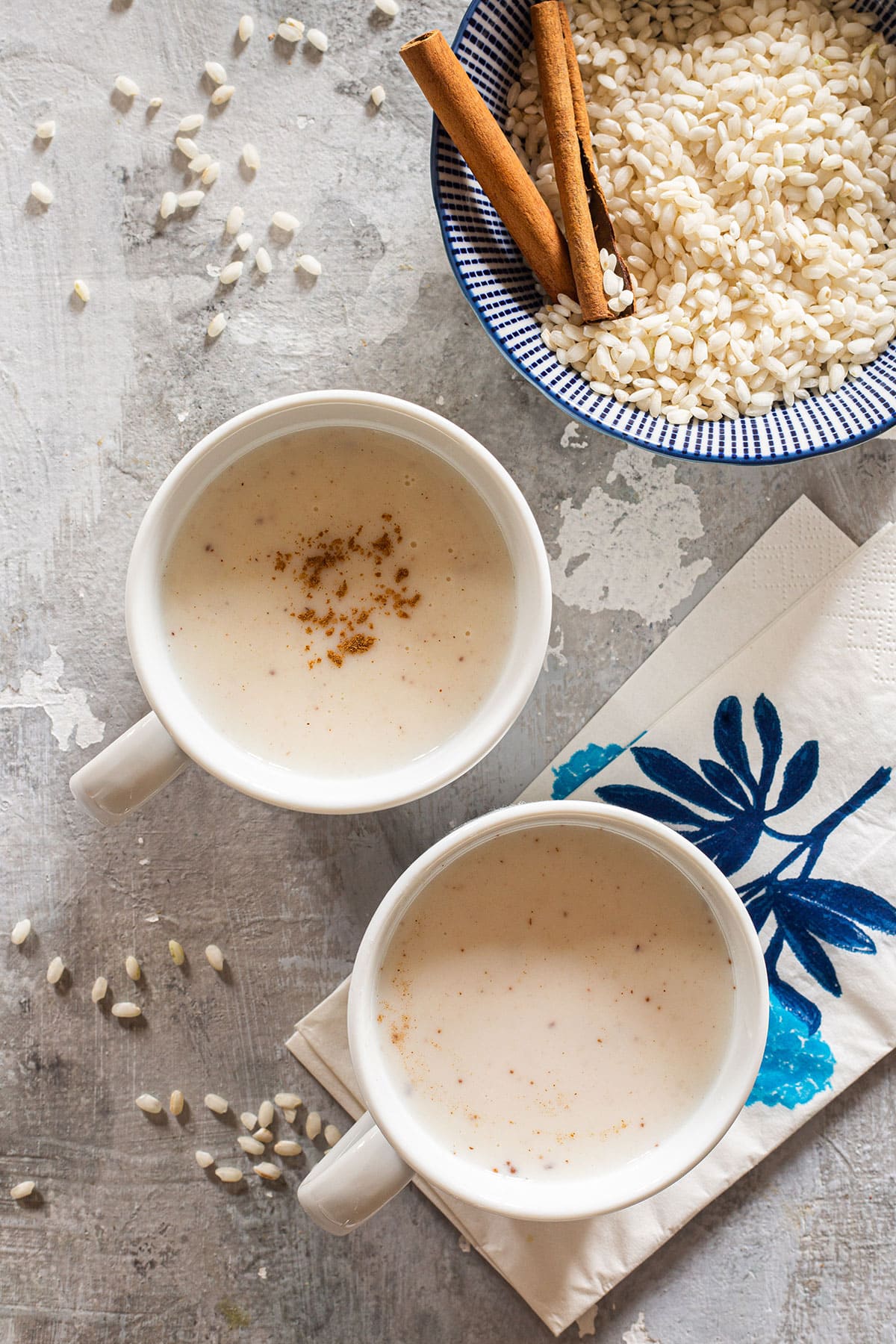 Rice atole, aka atole de arroz in two mugs with a bowl with rice and cinnamon on the side.