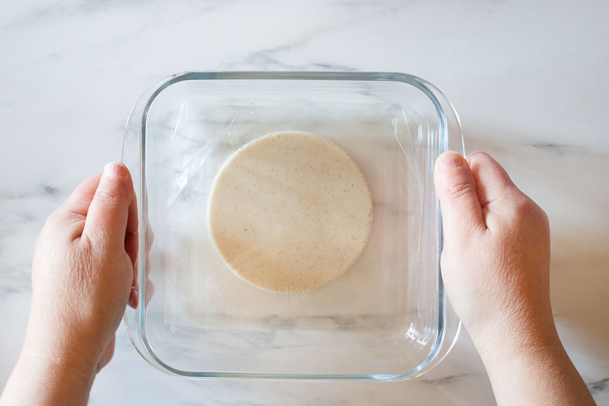 Pressing the masa dough with a heavy dish to make a disc.
