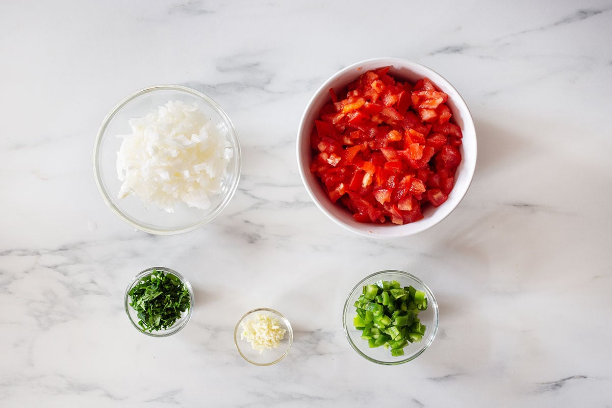 Diced and chopped tomatoes, onions, chilies, garlic, and parsley in bowls.