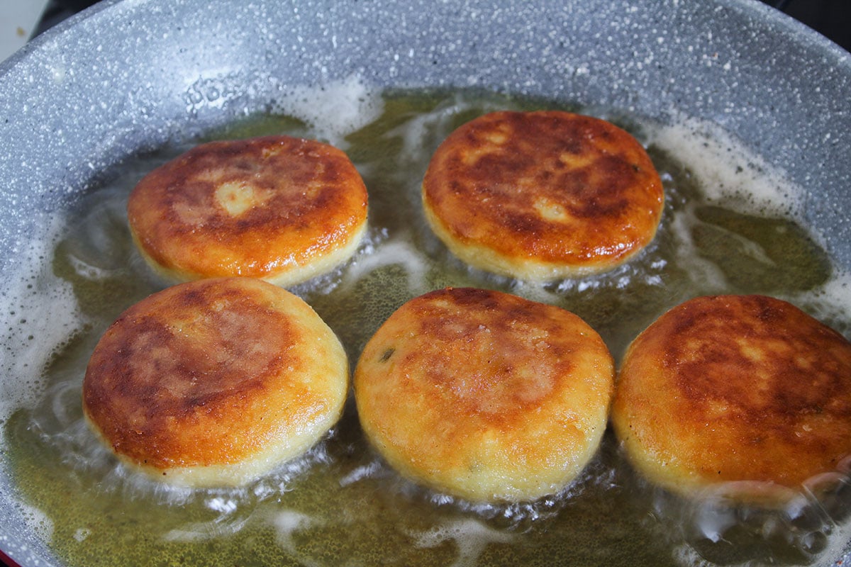 Tortitas de papa golden and crispy in a pan.