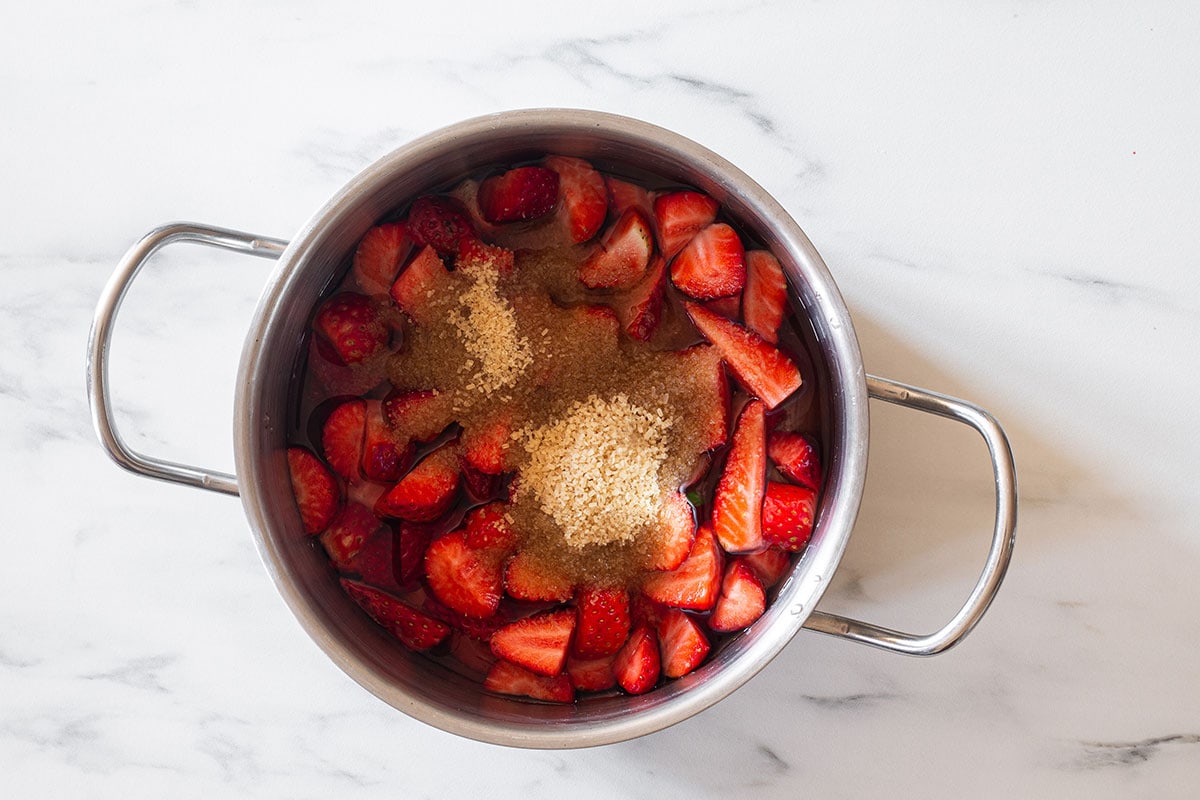 Quartered strawberries in a pot with brown sugar on top.