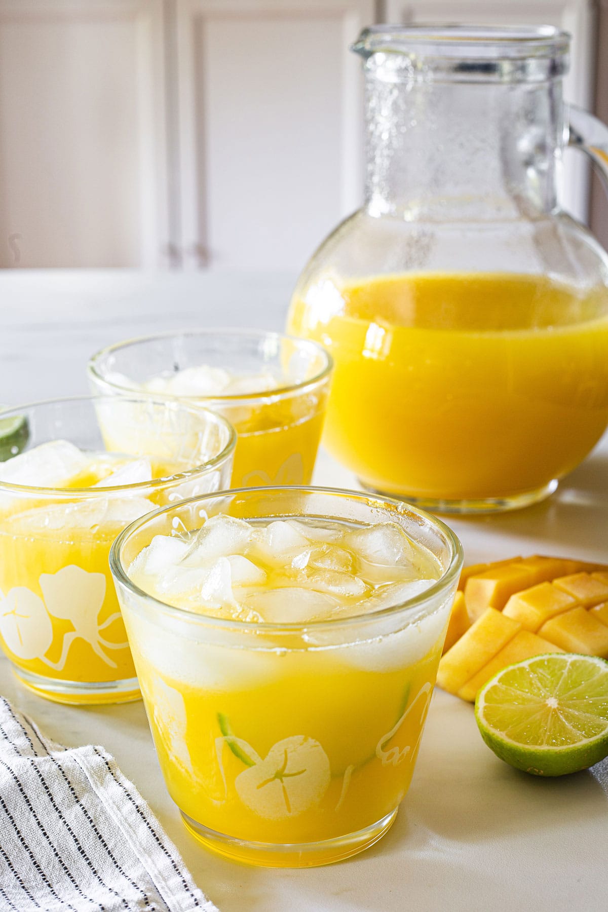 Agua de mango, also known as mango water in glasses with ice and a pitcher on the background.
