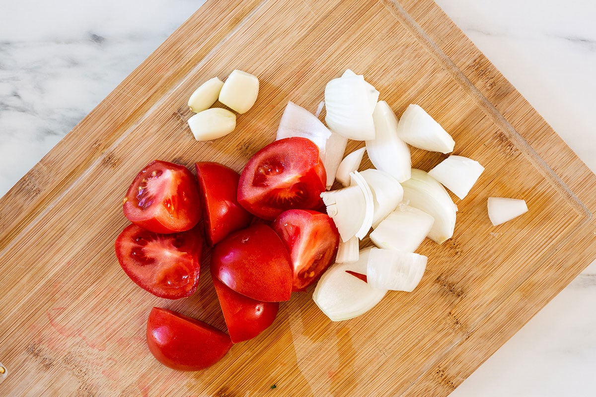 Quartered tomatoes and onions on a cutting board.