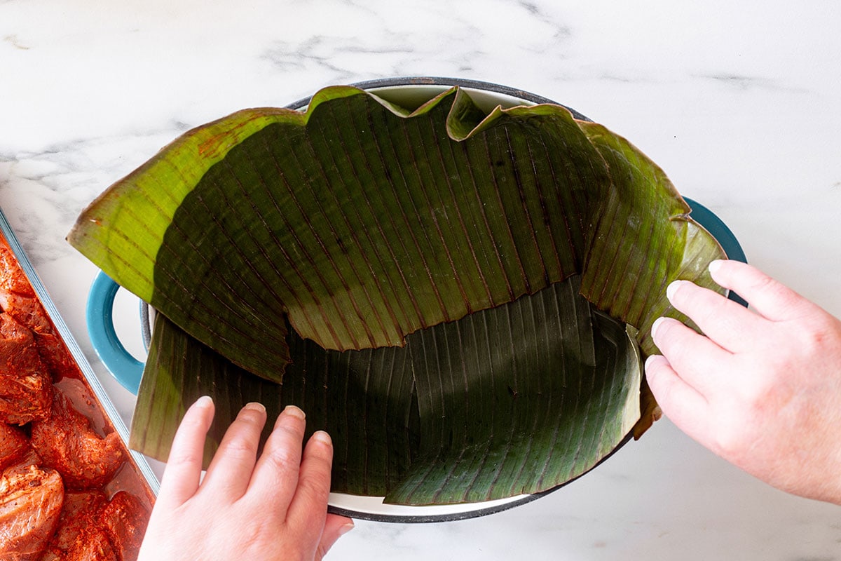 Lining a dutch oven pot with banana leaves to make cochinita pibil.