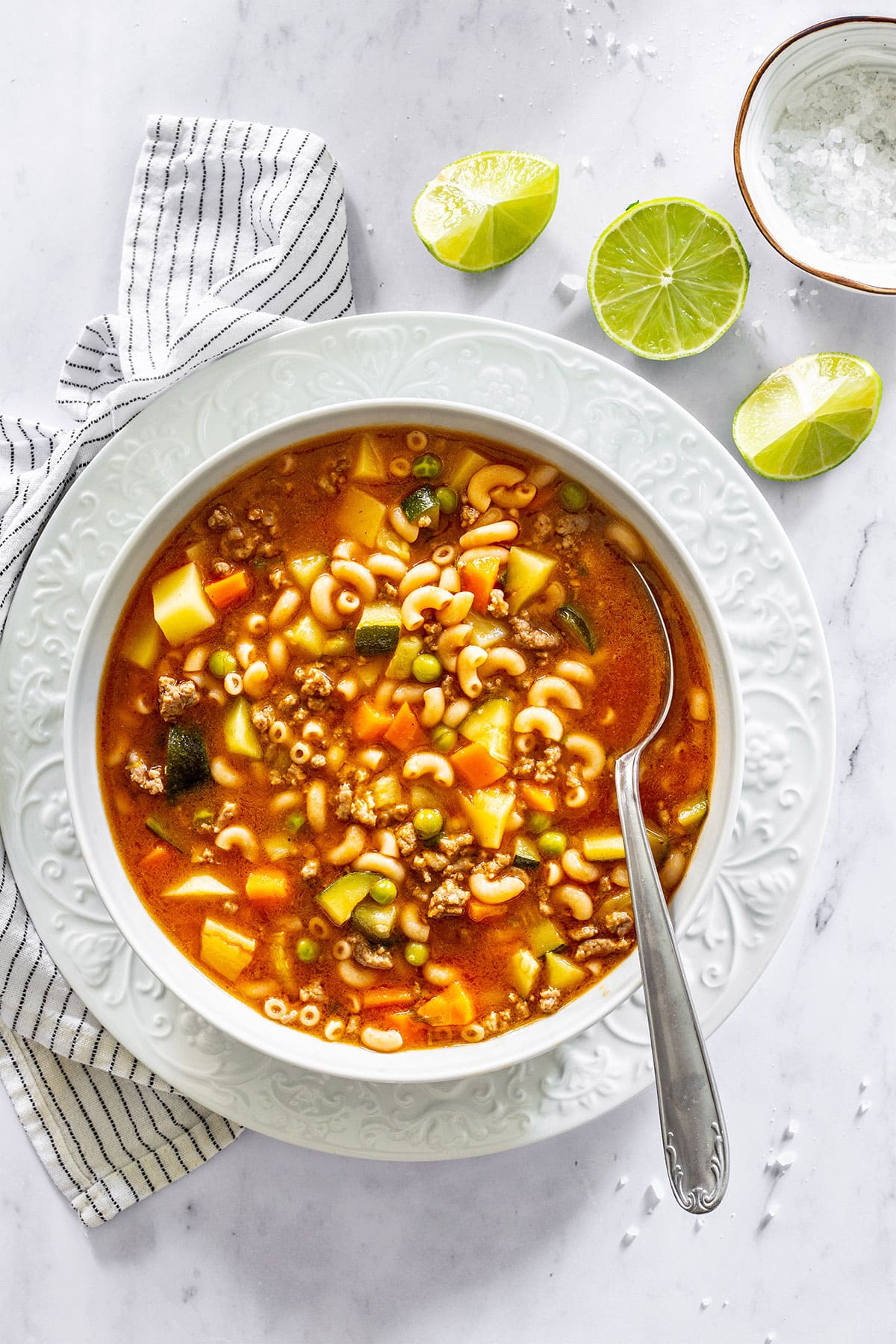 Mexican sopa de coditos served in a plate with some lime wedges on the side.