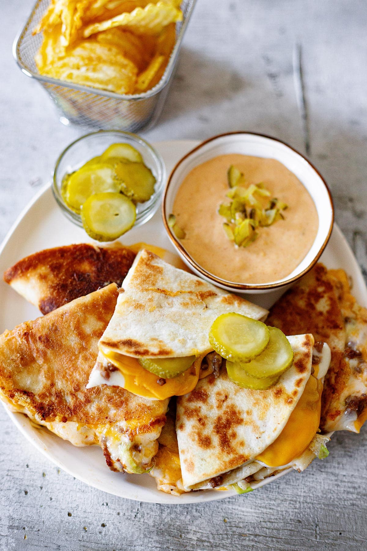 Big Mac quesadillas on a plate with a side of special sauce, pickles, and chips.