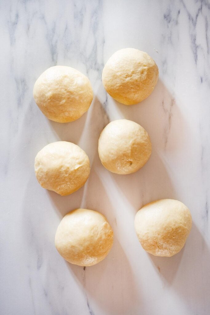 Six dough balls on a kitchen surface.
