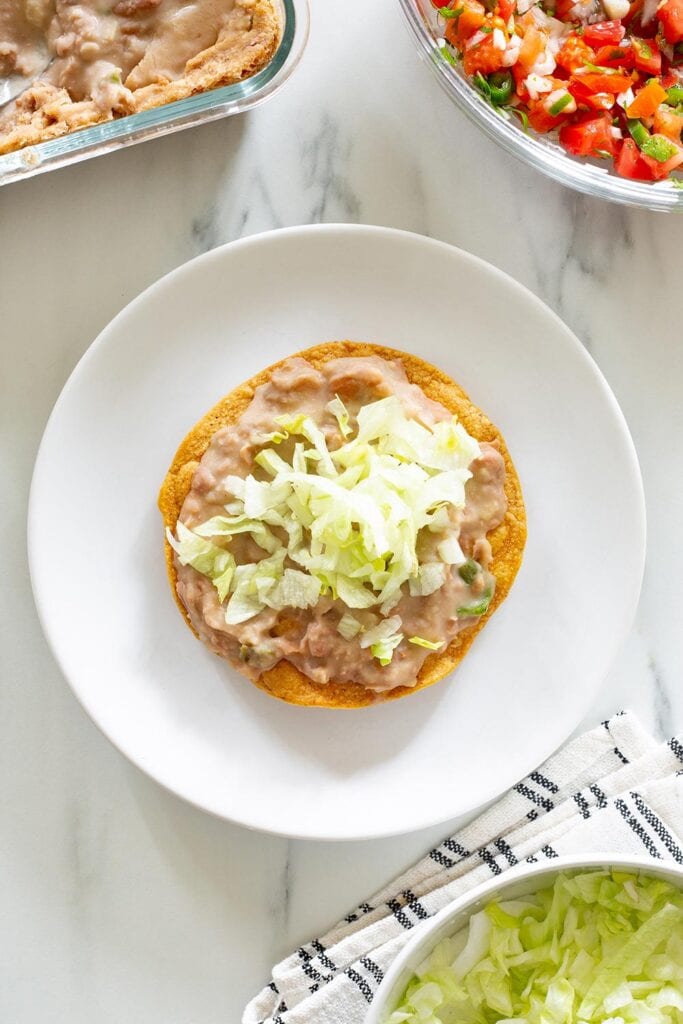 Tostada de frijoles with chopped lettuce on top.