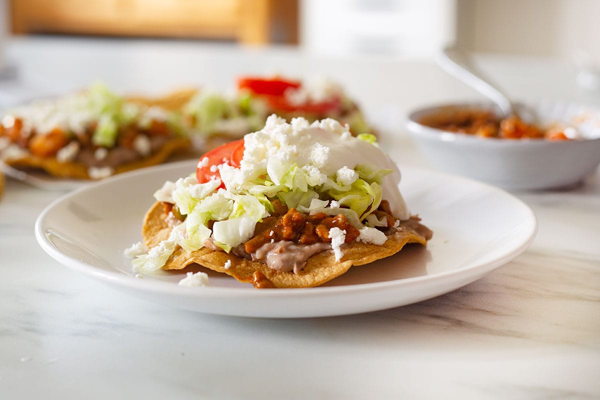 A fully assembled picadillo tostada with lettuce, tomatoes, crema, and cheese toppings.