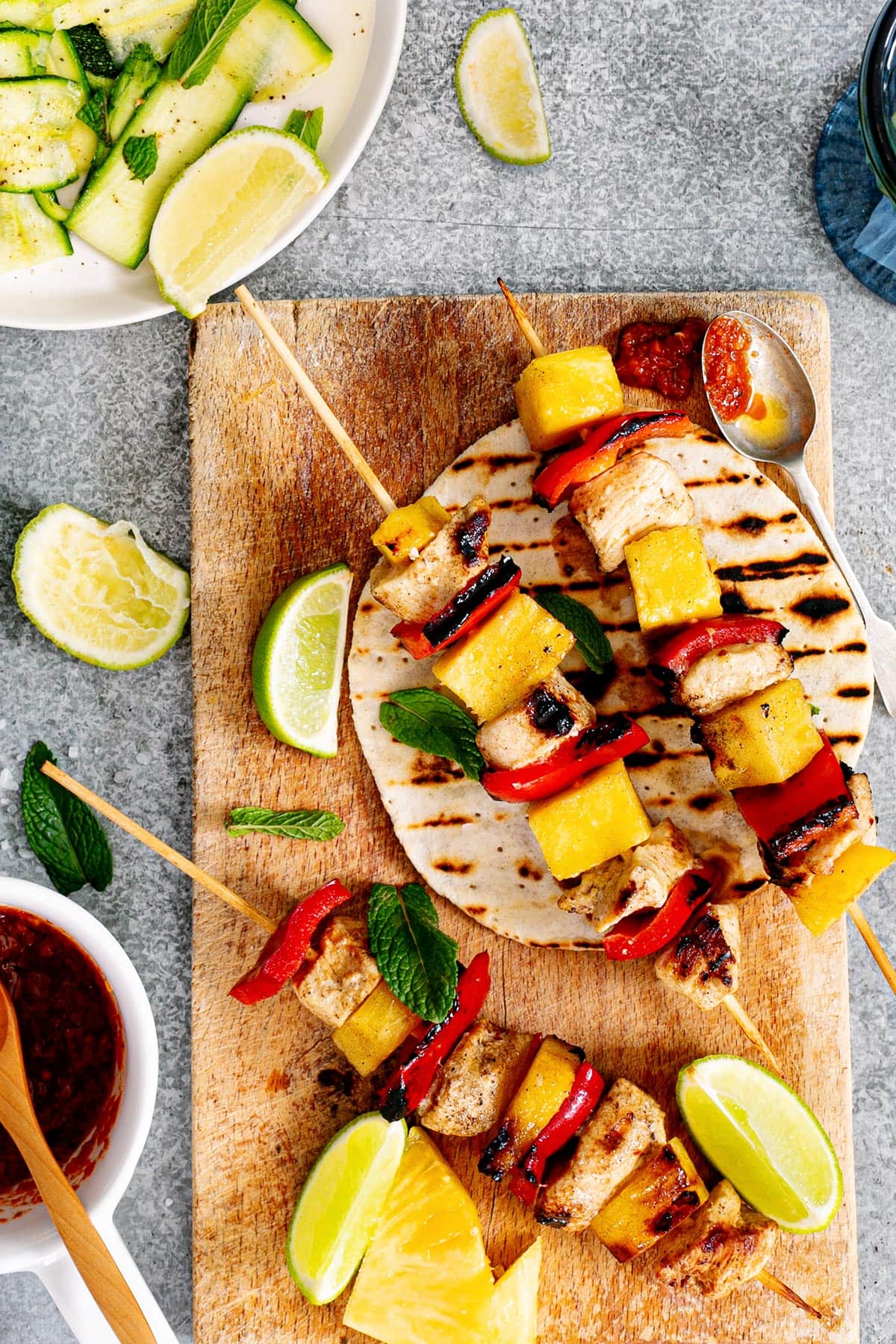 Brochetas de pollo, also known as Mexican chicken skewers placed on grilled tortillas, with lime wedges and salsa on the side.