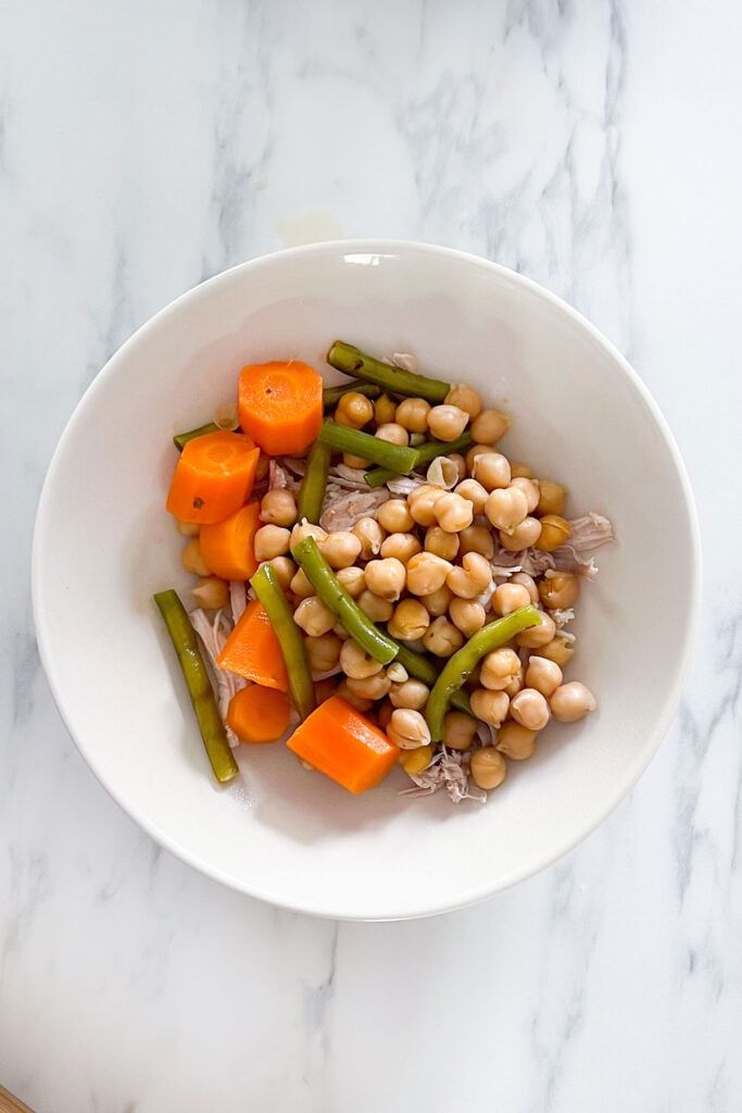 Chicken, chickpeas, and vegetables placed in a soup bowl.