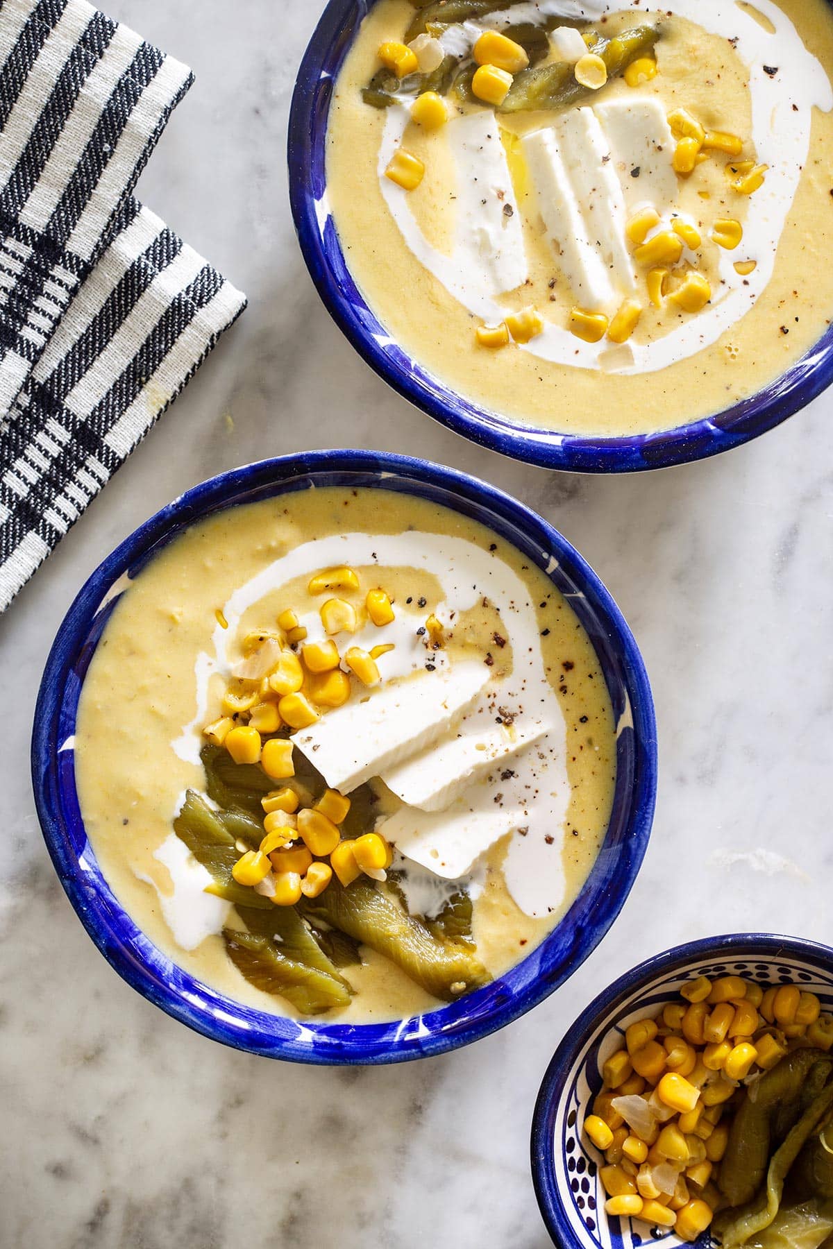 Crema de elote served in Mexican clay bowls and garnished with corn, roasted poblano peppers, cheese, and crema.