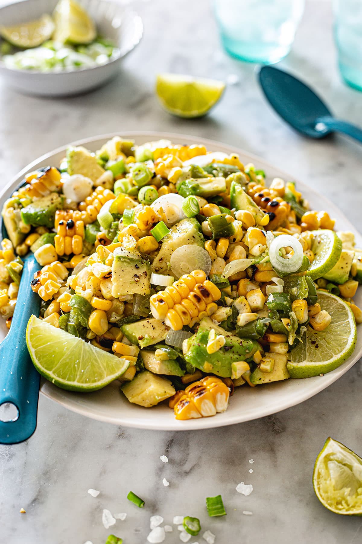 Salad with corn and avocado in a serving plate with some ingredients scattered around.