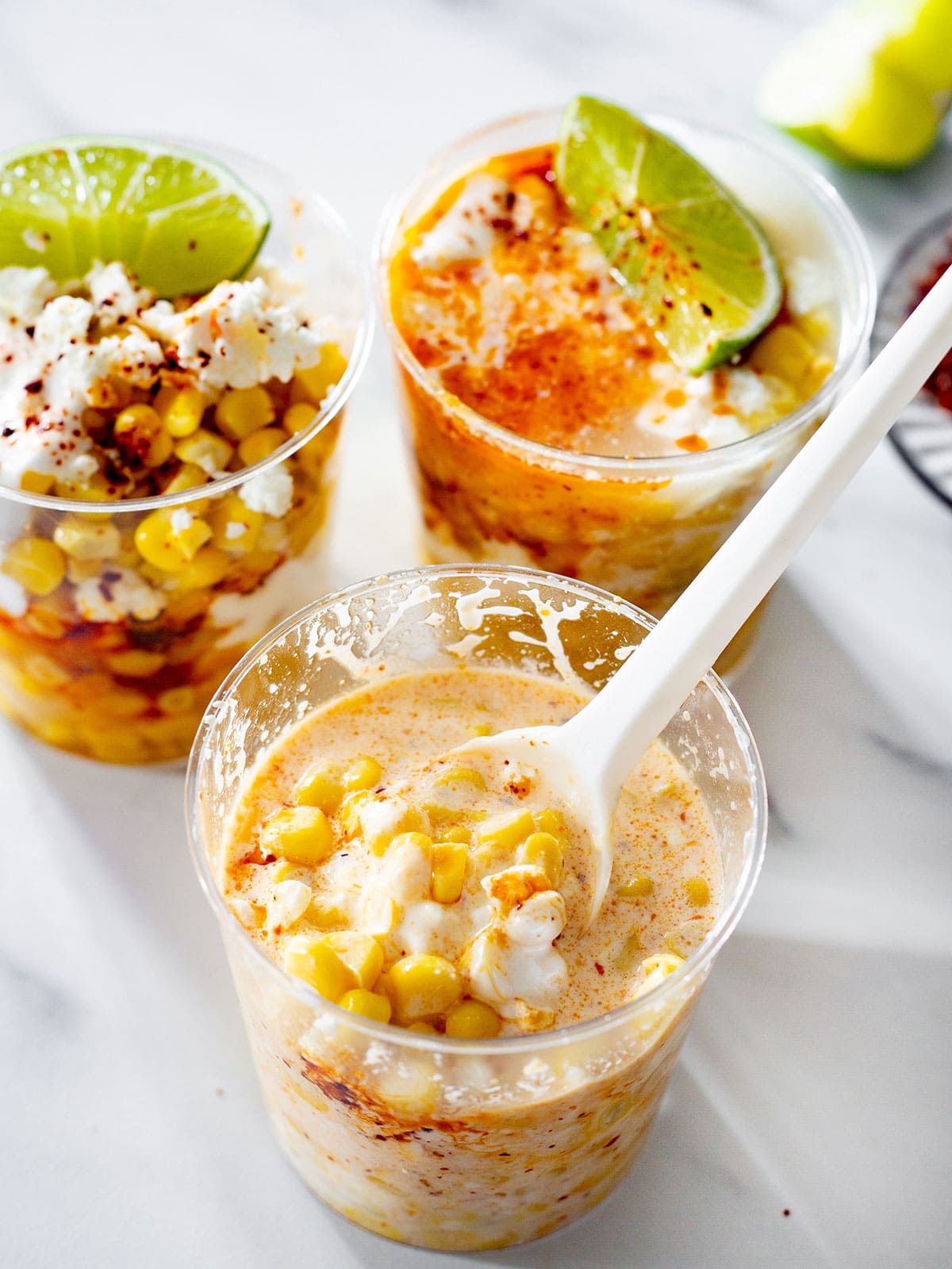 3 cups of elote en vaso, one of them mixed with a spoon.