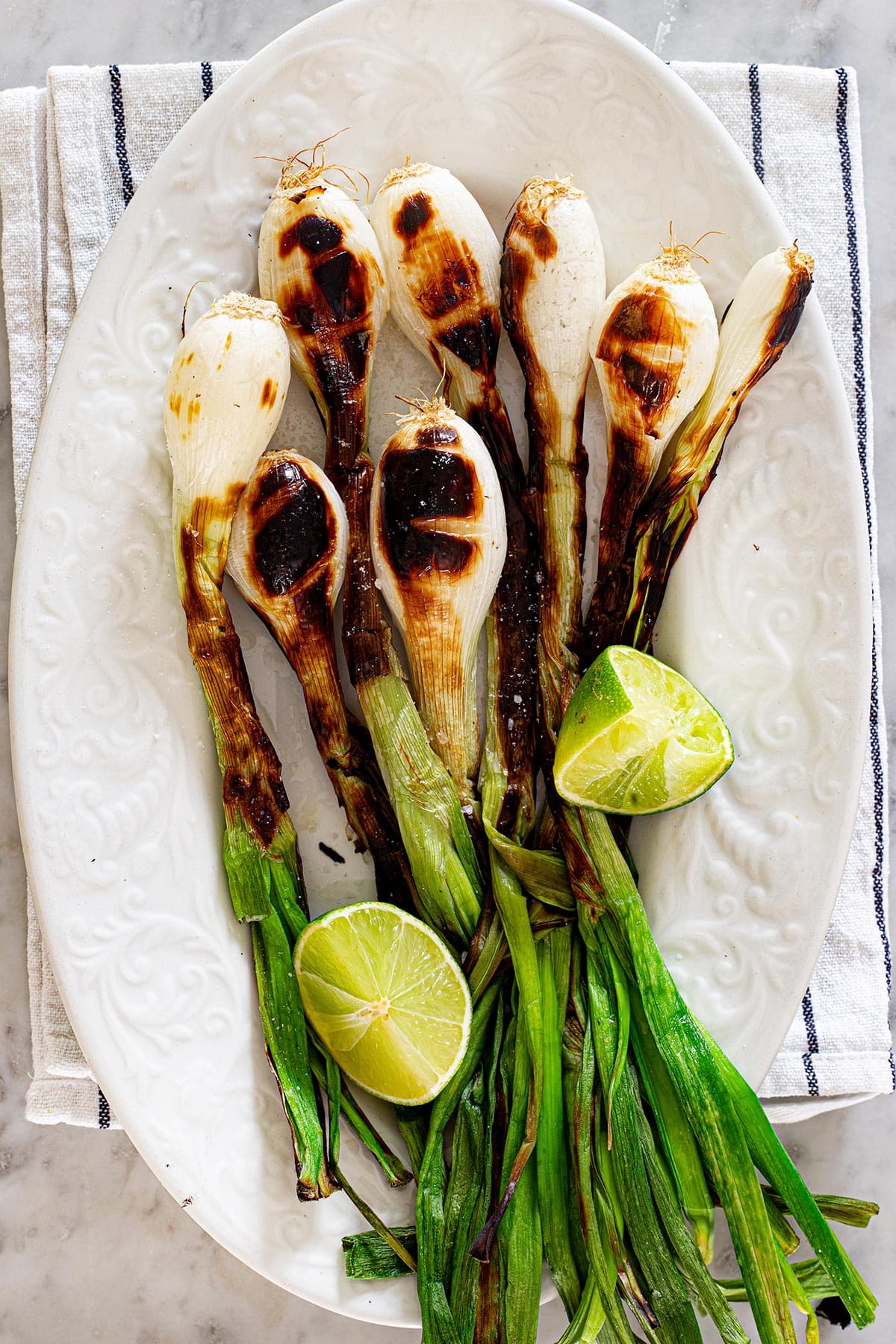 Mexican green onions, also known as cebollitas, placed in a white platter with lime wedges.