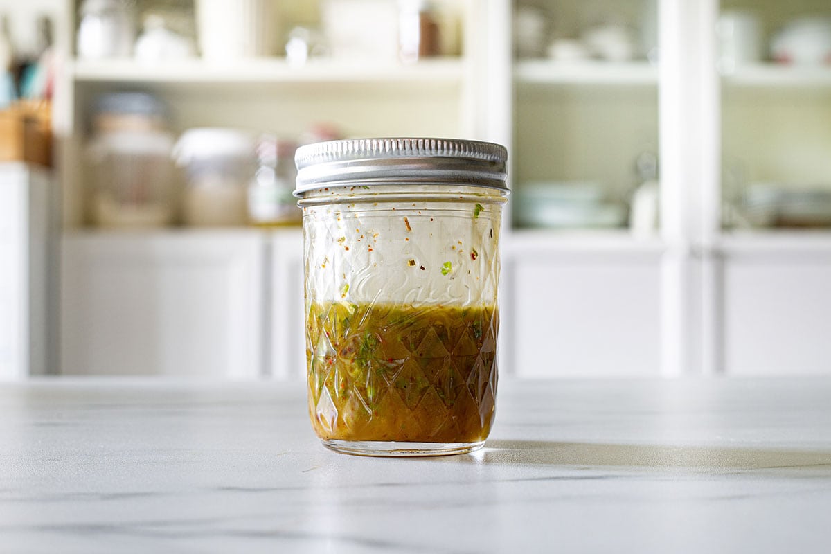 Emulsified dressing for the salad on a jar placed on a kitchen countertop.